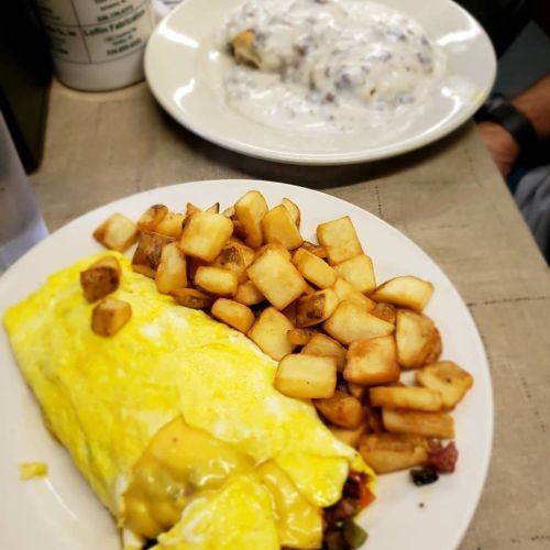 A plate with a cheese omelet, golden potatoes, and a side of biscuits smothered in gravy.