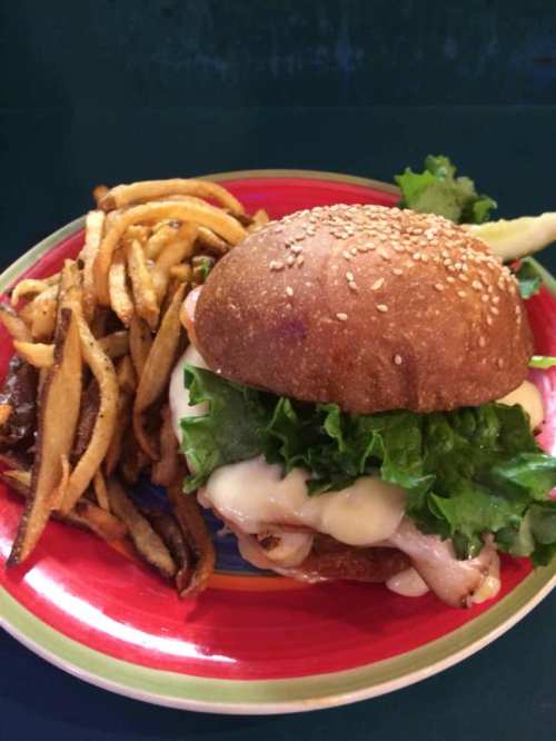A sesame seed bun burger with lettuce and sauce, served with a side of crispy French fries on a colorful plate.
