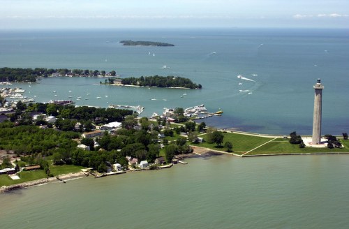 Aerial view of a coastal area with a lighthouse, boats, and lush greenery along the shoreline.