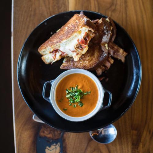 A plate with grilled cheese sandwiches and a small bowl of tomato soup, garnished with herbs.