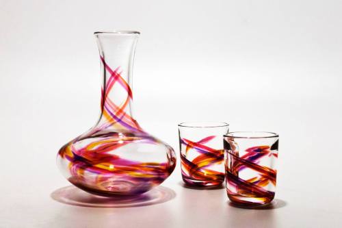 A colorful glass decanter with swirling patterns, accompanied by two matching glasses.