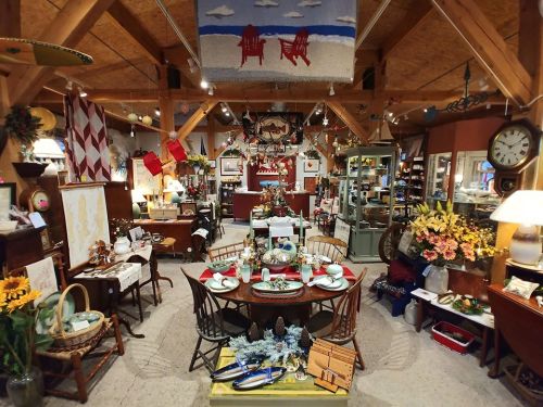 A cozy antique shop filled with vintage furniture, decor, and a dining setup, featuring nautical themes and warm lighting.