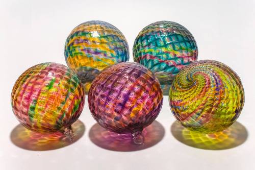 Five colorful, textured glass spheres arranged in a circle, reflecting light and casting vibrant shadows.