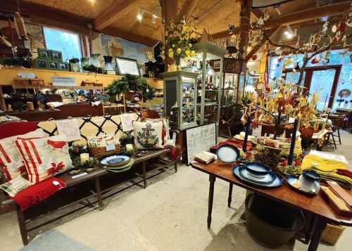 A cozy shop interior featuring rustic decor, a wooden bench with cushions, and a table set with plates and autumn decorations.