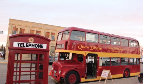 A red double-decker bus named "Queen Elizabeth" parked next to a traditional red telephone booth.