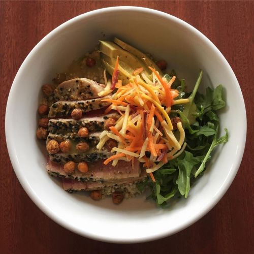 A bowl of sliced seared tuna, arugula, chickpeas, and shredded vegetables, drizzled with a light dressing.