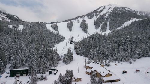 A snowy mountain landscape with ski slopes, a ski lift, and a lodge surrounded by evergreen trees.