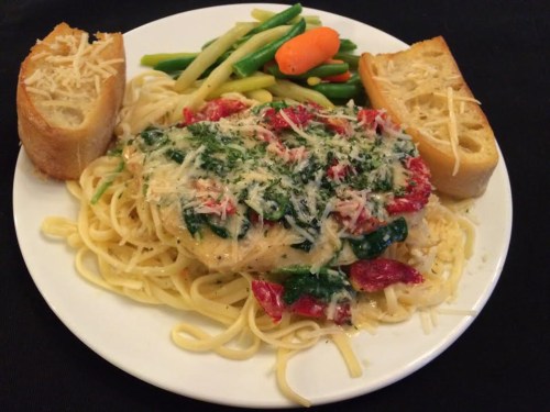A plate of pasta with chicken, spinach, and tomatoes, served with garlic bread and a side of mixed vegetables.