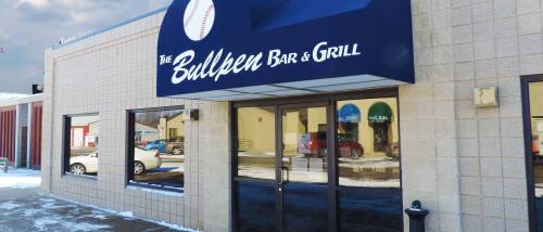 Exterior view of The Bullpen Bar & Grill, featuring a blue awning and snow-covered ground.