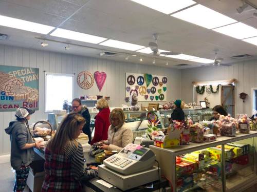 A busy candy shop with customers at the counter, colorful displays, and peace-themed decorations on the walls.
