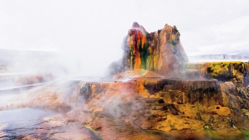 A colorful geothermal feature with steam rising, showcasing vibrant mineral deposits in a natural landscape.