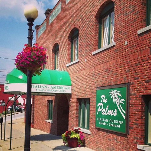 Exterior of The Palms restaurant featuring a green awning, brick facade, and hanging flower baskets.
