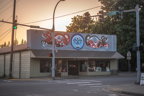 A corner building with Indigenous art on the facade, featuring animals and a blue circle, at a traffic intersection.