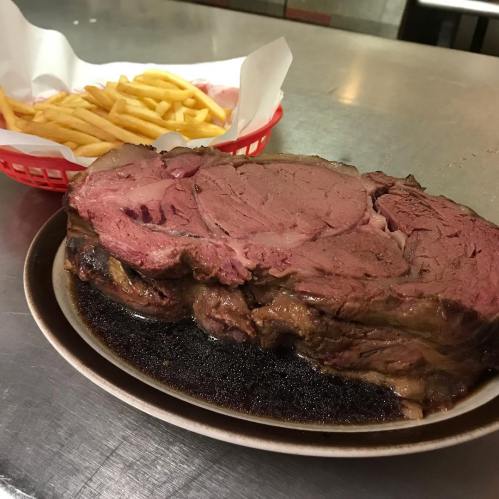 A plate of juicy prime rib served with a side of golden French fries in a red basket.