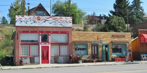 Colorful storefronts with unique architectural details, featuring a mural, an antiques shop, and a welcoming atmosphere.