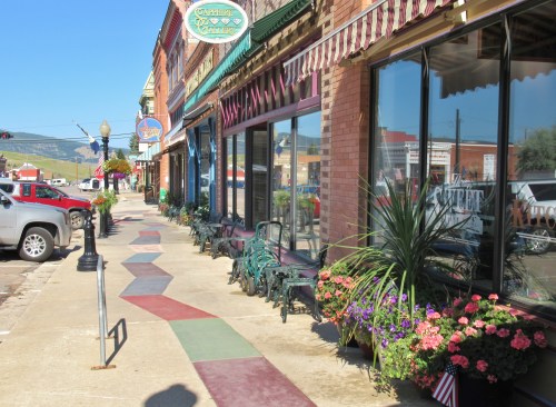 Colorful sidewalk with geometric patterns, lined by shops and flowers in a quaint town setting.