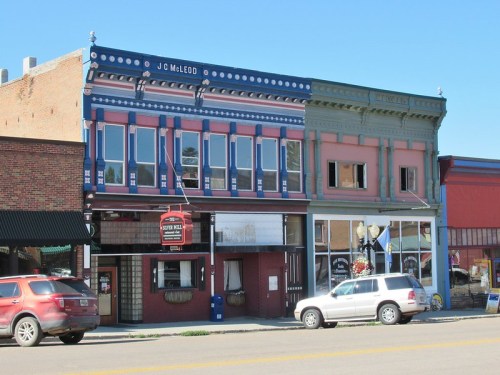Historic buildings with colorful facades, featuring shops and a restaurant, set against a clear blue sky.