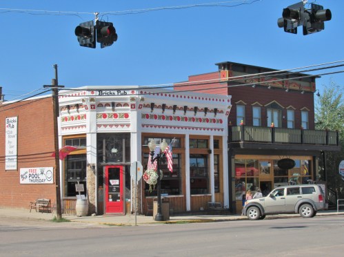 A charming pub with decorative trim, flags, and a sign for free food Thursday, located on a busy street corner.