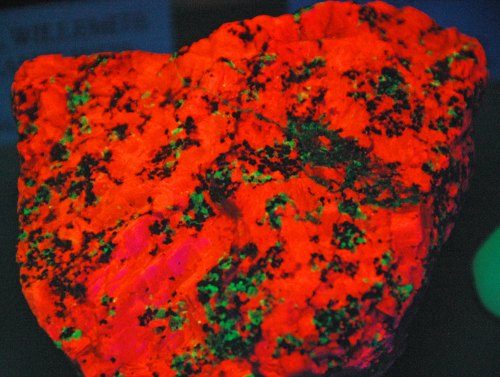 A vibrant, glowing rock displaying bright red and green colors under ultraviolet light.
