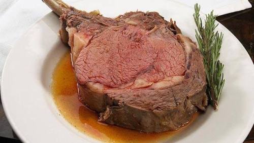 A juicy prime rib steak served on a plate with a sprig of rosemary and a rich, savory sauce.
