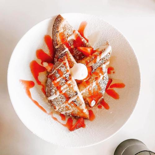 A plate of French toast topped with strawberries, whipped cream, and a drizzle of sauce.