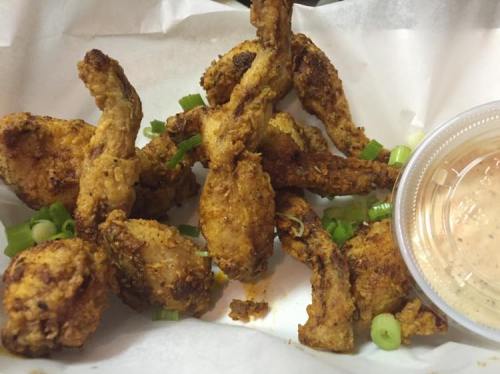 A serving of crispy fried chicken wings garnished with green onions, accompanied by a small cup of dipping sauce.