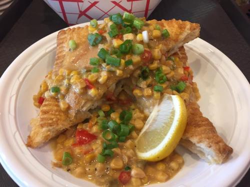 A plate of flaky pastry topped with corn, peppers, and green onions, served with a lemon wedge.