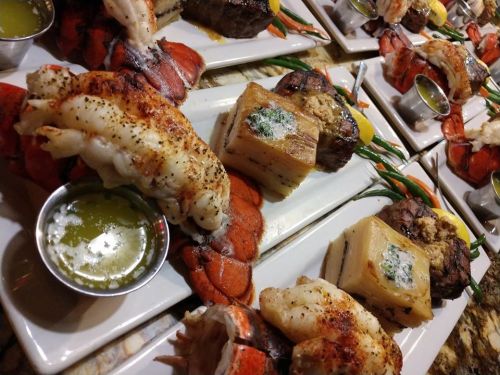 Plates of gourmet seafood and steak, featuring lobster, shrimp, and a rich sauce, beautifully arranged.