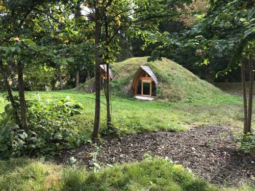 A unique, grassy dome-shaped structure nestled among trees in a lush green landscape.