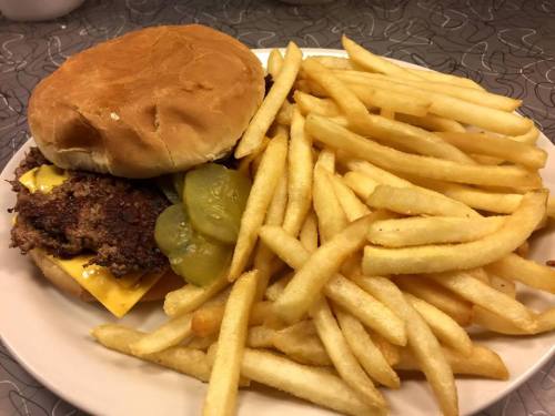 A plate with a cheeseburger topped with pickles and a side of golden French fries.