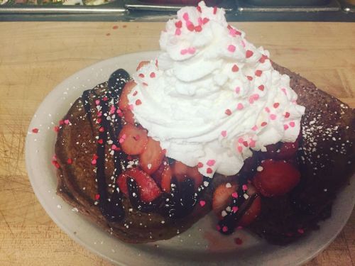 A plate of pancakes topped with whipped cream, strawberries, chocolate sauce, and colorful sprinkles.