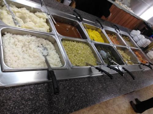 A buffet with various dishes, including rice, gravy, yellow rice, and vegetables in metal trays on a countertop.