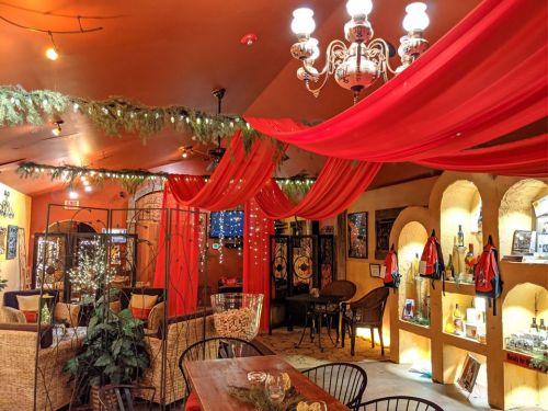 Cozy interior of a cafe with red drapes, warm lighting, and decorative shelves, creating an inviting atmosphere.