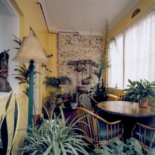 A cozy sunroom with yellow walls, a stone wall feature, plants, a round table, and a lamp.