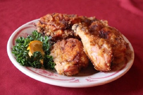 A plate of crispy fried chicken pieces garnished with parsley and a slice of orange on a red tablecloth.