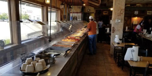 A man serves himself at a buffet in a casual restaurant with a variety of food options displayed.