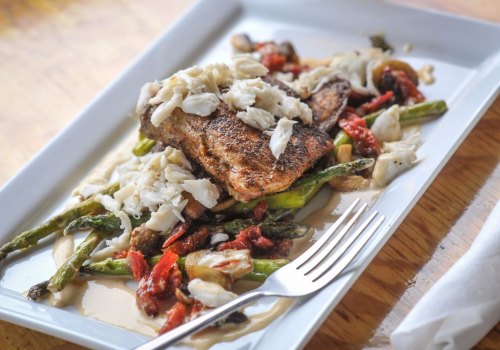 A plate of seasoned fish topped with crab, served on a bed of asparagus and sun-dried tomatoes in a creamy sauce.