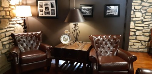 Cozy seating area with two brown leather chairs, a lamp, and a wooden table adorned with decorative items and framed photos.