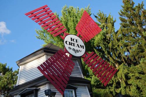 A whimsical windmill sign with red blades and a central "Ice Cream" logo, set against a backdrop of green trees.