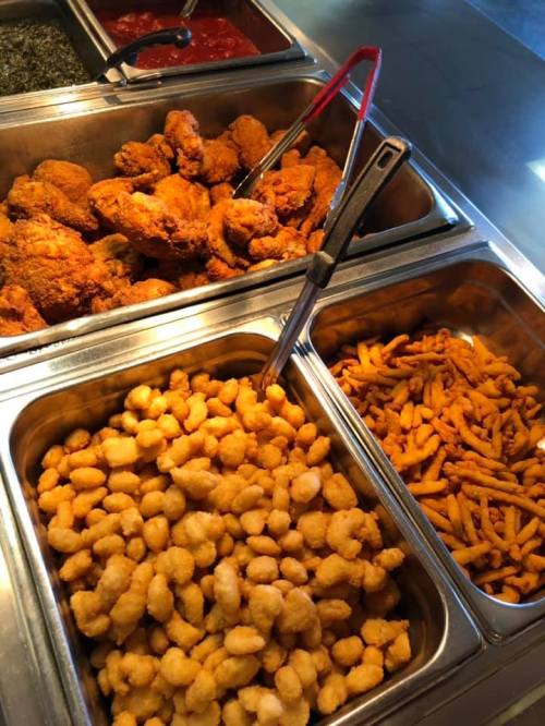A buffet display featuring crispy fried chicken, golden popcorn shrimp, and seasoned fries in metal trays.