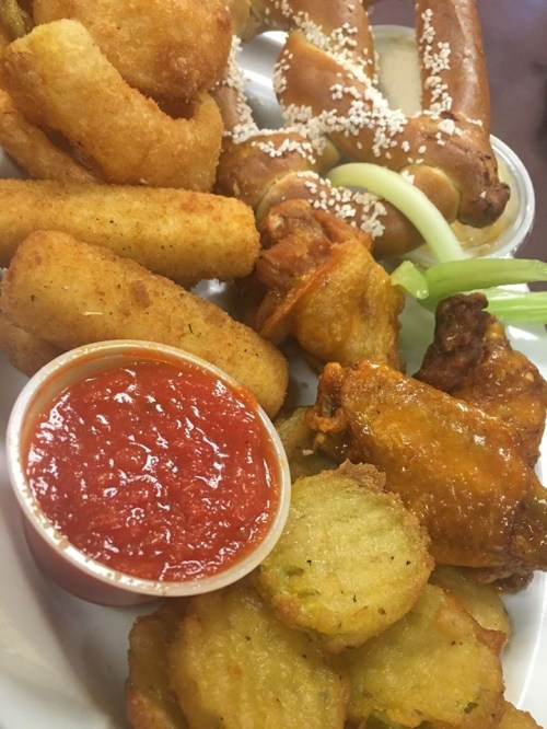 A platter of assorted fried foods including wings, mozzarella sticks, and pretzel bites, served with marinara sauce.