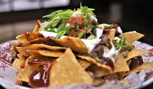 A close-up of a plate of nachos topped with cheese, sour cream, salsa, and green onions.