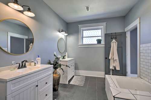 Modern bathroom featuring a double vanity, round mirrors, gray walls, and a soaking tub with a plant accent.