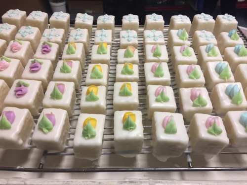 A tray of small, square desserts topped with colorful icing decorations in pastel shades.