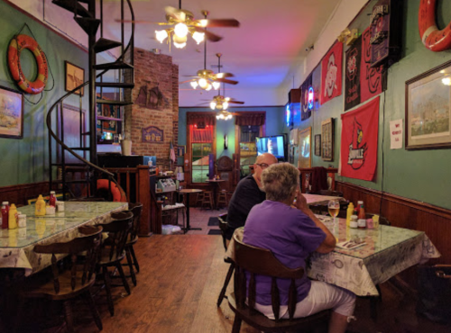 Cozy restaurant interior with spiral staircase, tables, and colorful decor, featuring patrons enjoying their meals.