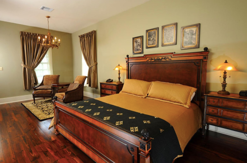Cozy bedroom featuring a wooden bed, warm yellow bedding, armchairs, and elegant decor with soft lighting.