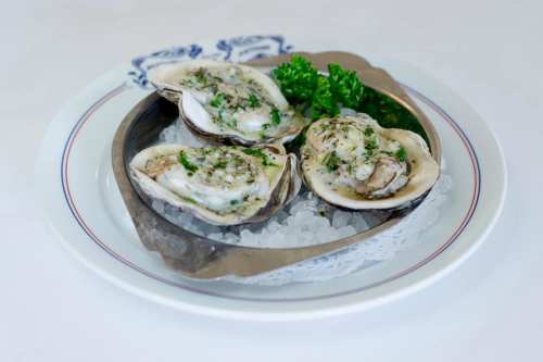 A plate of three oysters on ice, garnished with parsley, served in a silver dish.
