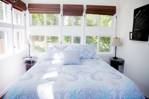Bright bedroom with a patterned bedspread, two lamps, and large windows overlooking greenery.