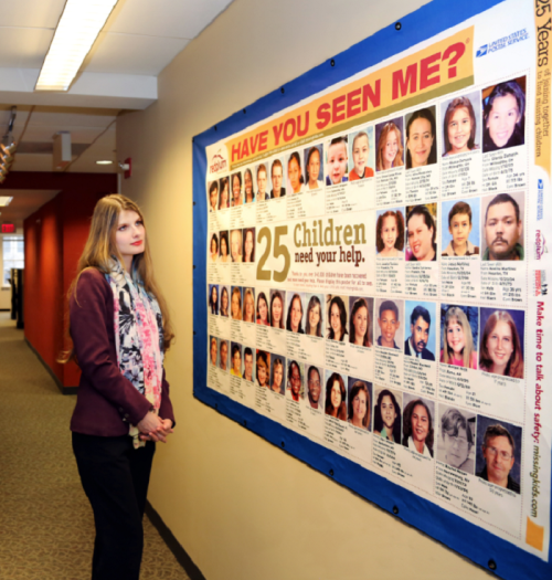 A woman stands beside a poster featuring photos of 25 missing children, seeking public assistance in their search.