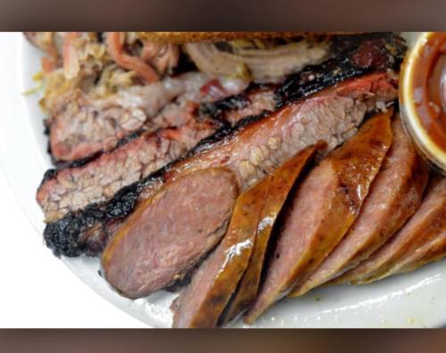 Close-up of sliced smoked brisket and sausage on a plate, served with barbecue sauce.